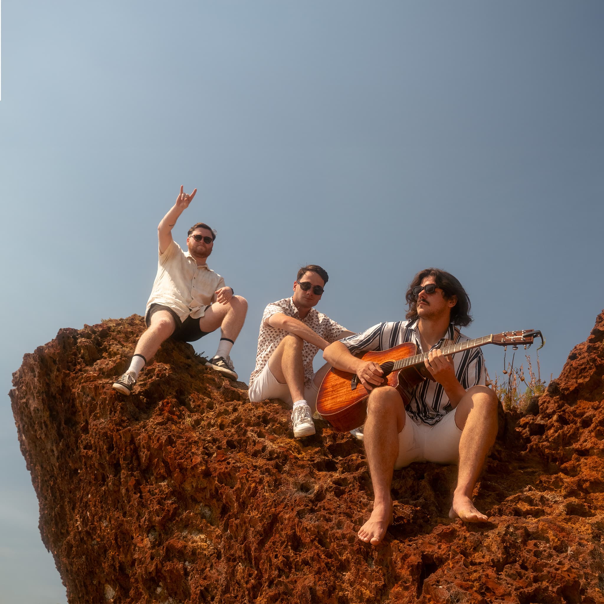 Sam and friends sitting on a rocky coast with a guitar